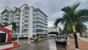Een meerlaags woongebouw met balkons, een geplaveid voetpad en palmbomen.