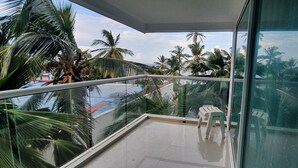 Een balkon met glazen hekwerk, palmbomen en een heldere lucht.