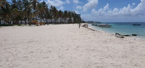A beach with white sand, palm trees, and boats in the water.