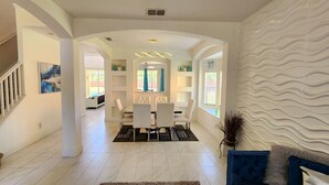 Un vaste espace de vie comprenant un escalier, une table à manger avec des chaises et un mur décoratif.