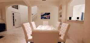 Ein Essbereich mit einem weißen Tisch und Stühlen, einem Gemälde an der Wand und einer Treppe, die in einen anderen Raum führt.