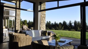 A modern living room with a large glass door leading to a patio, wicker furniture, and a view of a green landscape.