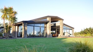 A modern house with large glass windows, stone pillars, and a well-maintained lawn. - Matapouri and Poor Knights Spectacular Coastal Views - Aroha Luxury Guest Suite (Tutukaka)