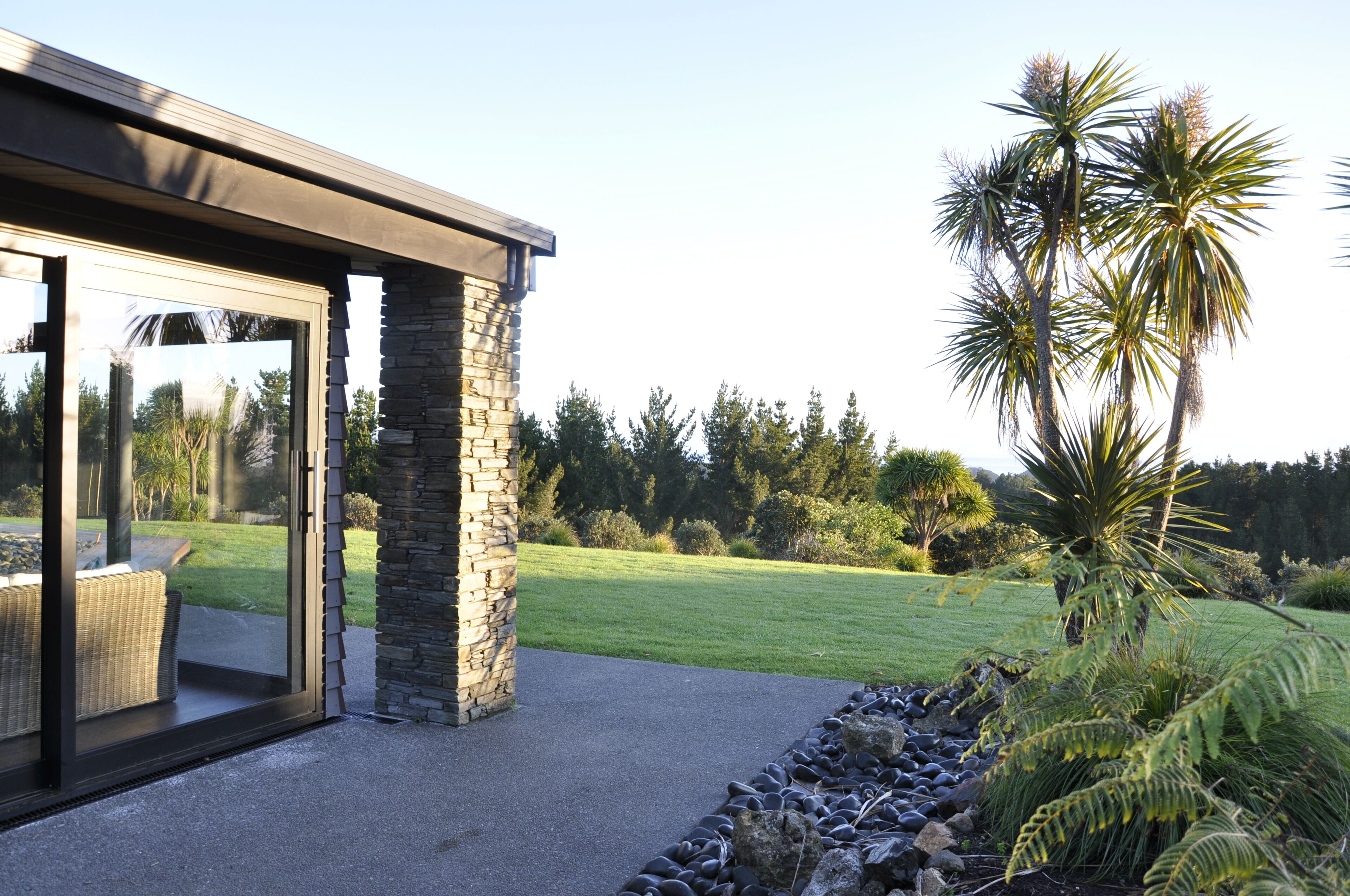 A modern building with a stone exterior, large glass doors, and a view of a well-maintained lawn and trees.