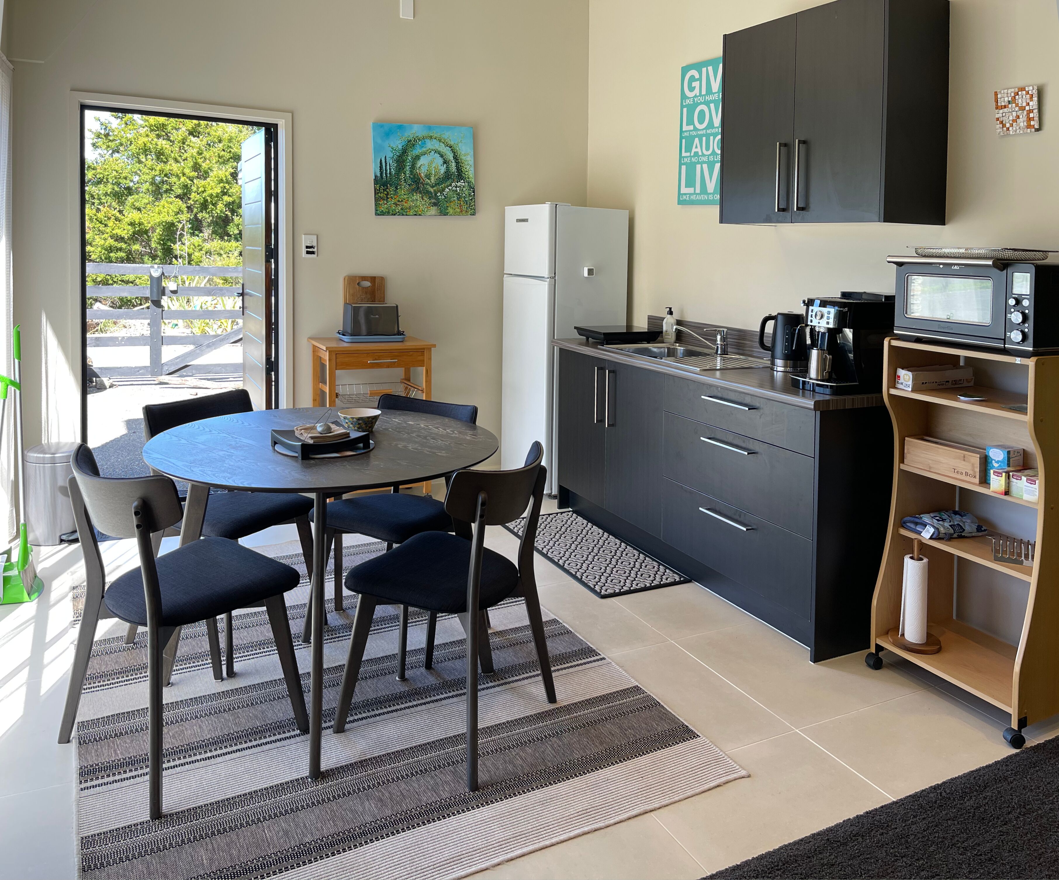 A modern kitchen with a dining area, featuring a round table, chairs, a refrigerator, a microwave, and a coffee maker.