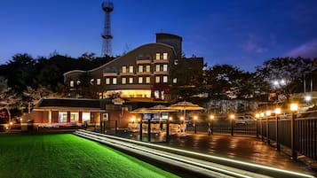 Hotel features a curved roof and multiple balconies, with a well-manicured lawn and covered parking area.