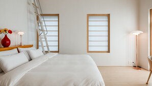 Un dormitorio moderno con una cama, una escalera, un jarrón rojo y dos lámparas de pie.