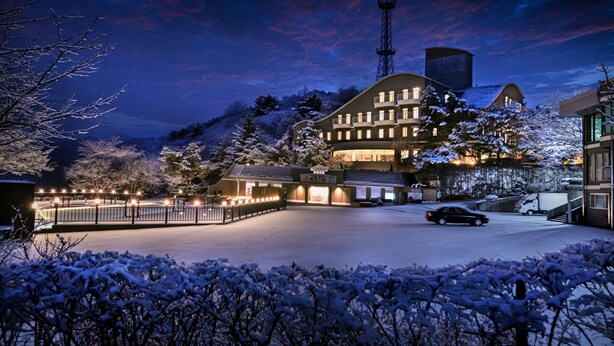 Un hotel con varios pisos, un estacionamiento y un paisaje cubierto de nieve.