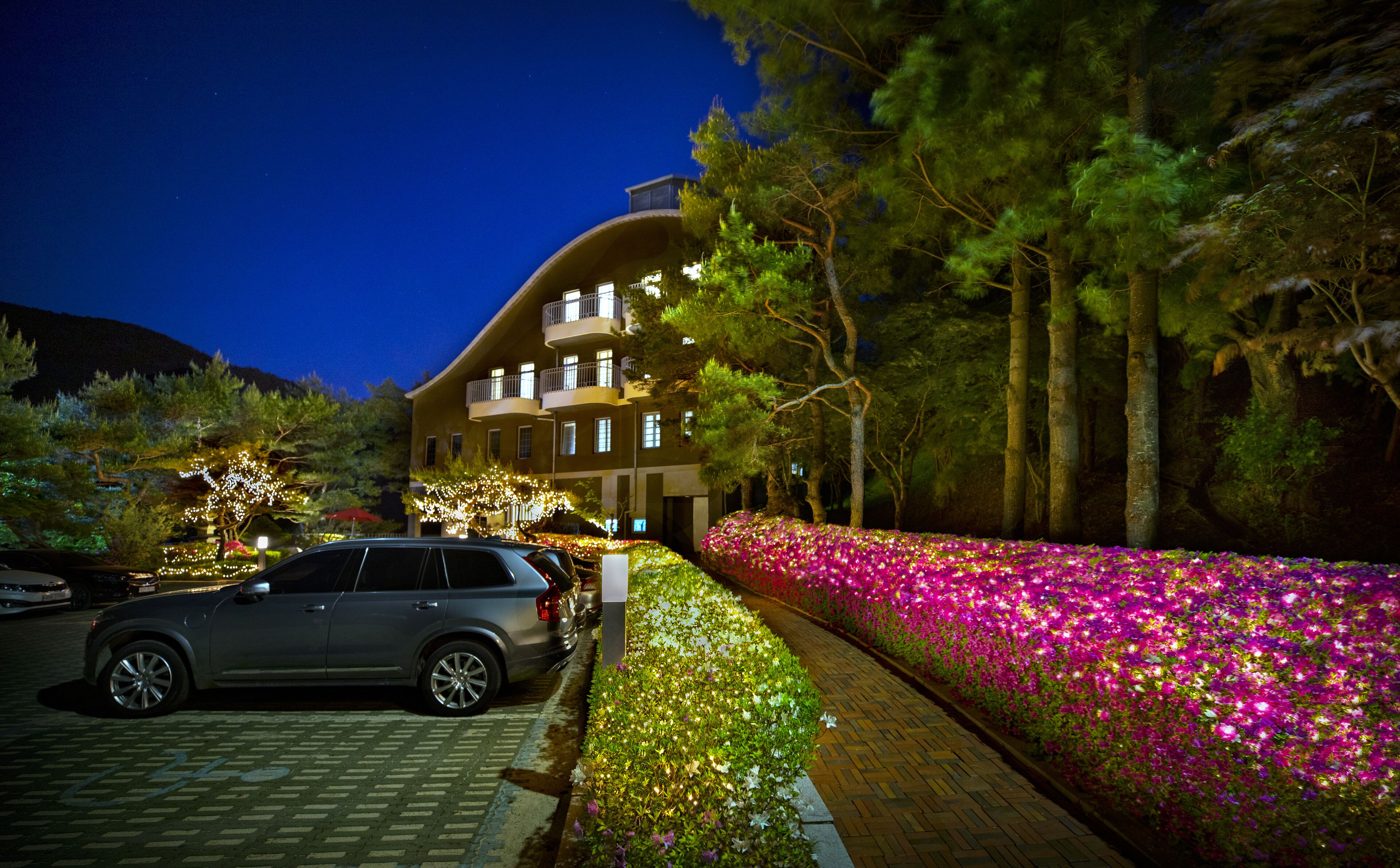 A hotel with a curved facade, multiple balconies, and a landscaped garden with flowers.