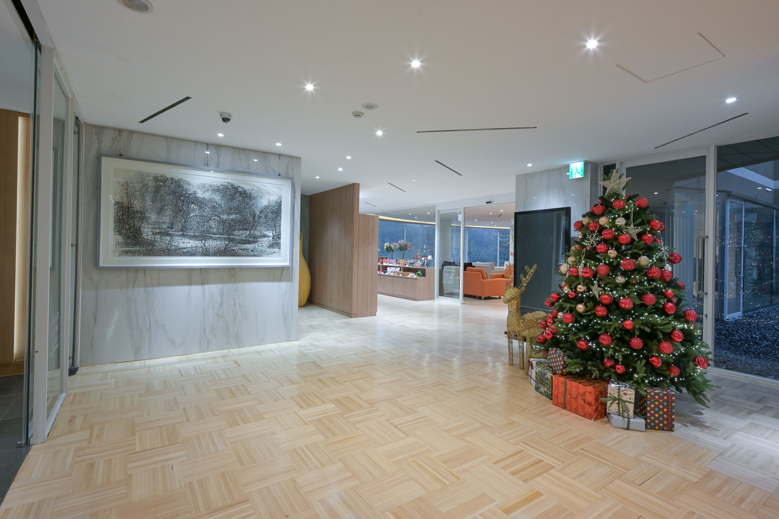 A modern hotel lobby with a large Christmas tree, wooden flooring, and a framed artwork on the wall.