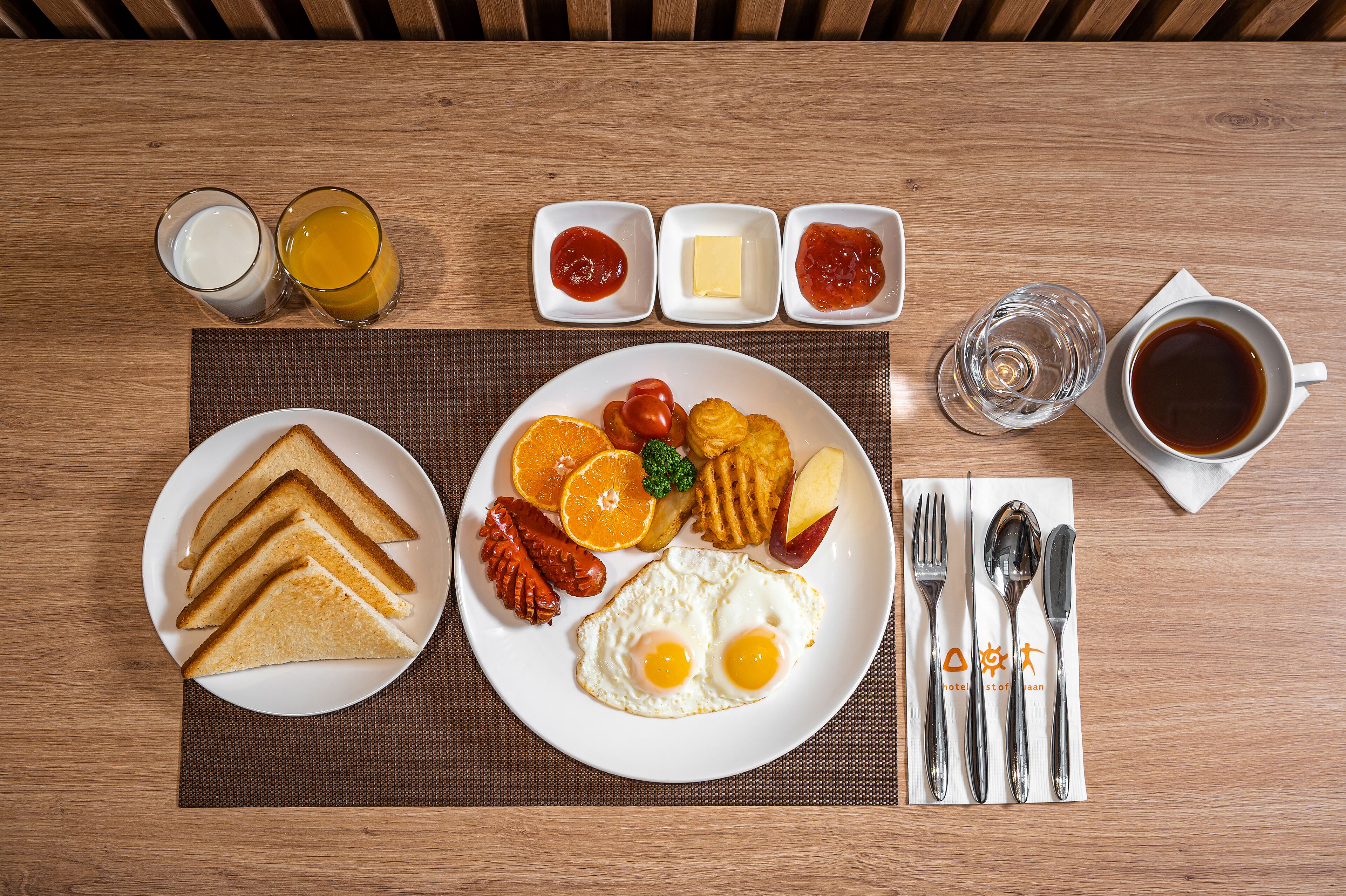 A breakfast plate with toast, eggs, and fruit, accompanied by condiments and a cup of coffee on a wooden table.
