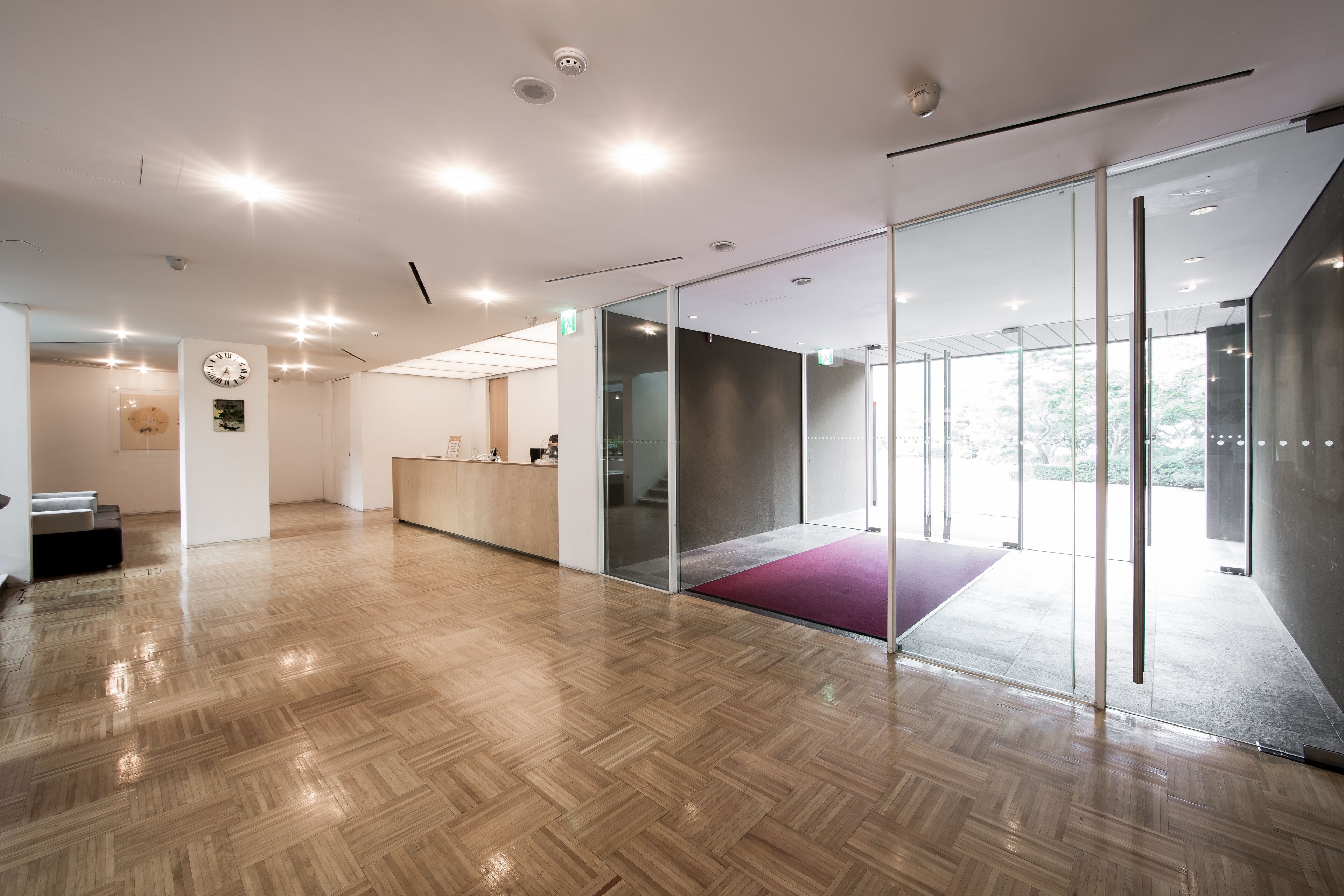 Un espace de bureau moderne avec un plancher en bois, des cloisons en verre, un comptoir d’accueil et une horloge au mur.