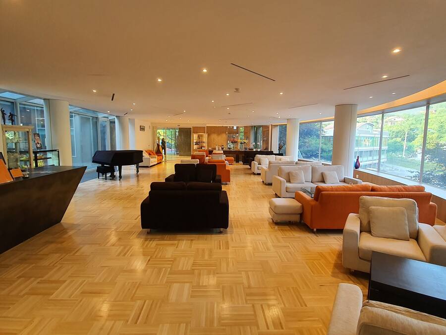 A spacious lobby with a piano, seating areas, and large windows offering a view of greenery.