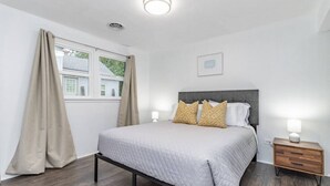 Un dormitorio con una cama, dos lámparas de noche, una mesita de noche, una ventana con cortinas y una lámpara de techo.