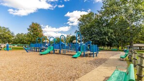 Un parque infantil con toboganes y estructuras para escalar, rodeado de árboles y bancos.