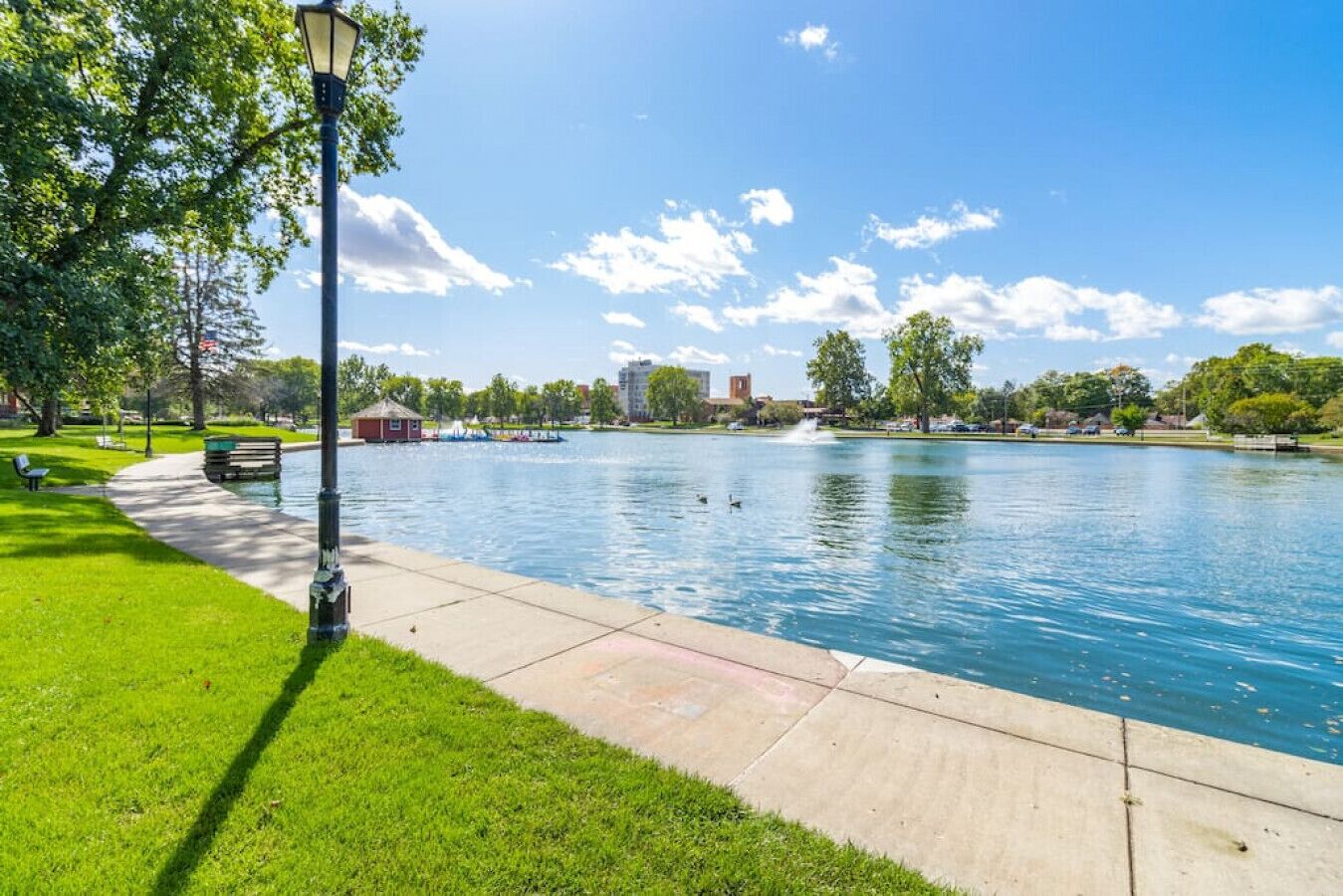 Un parc avec un plan d’eau paisible, un sentier pédestre et un lampadaire.