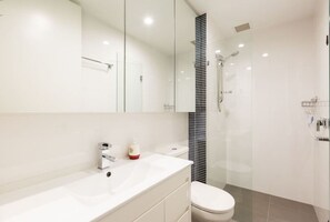 Features a sleek vanity, large mirror, white sink, toilet, and glass-enclosed shower.