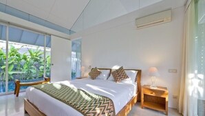 A modern bedroom with a large bed, a bedside table, and a view of greenery outside.