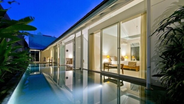 A modern hotel with a glass-enclosed pool, a well-lit interior, and a view of the surrounding greenery.