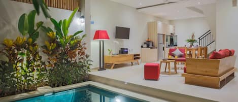 Una sala de estar moderna con piscina, muebles de madera y una lámpara roja.