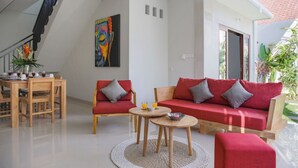 A modern living room with a staircase, red sofas, wooden coffee table, and a colorful abstract painting. - Villa Double 6 (Seminyak)