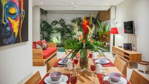 A dining area with a wooden table set for four, surrounded by red cushions and a large vase with tropical flowers. - Villa Double 6 (Seminyak)