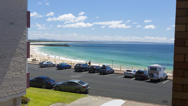 A parking lot with cars and a camper trailer, overlooking a beach and ocean. - Aloha Beachside (Forster)