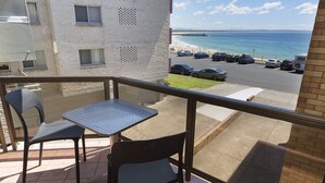 A balcony with two chairs and a table, overlooking a parking area and a beach. - Aloha Beachside (Forster)