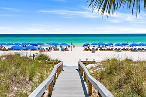 A wooden boardwalk leading to a beach with blue umbrellas and lounge chairs. - Beachfront ground-floor condo with a private patio, access to the beach and pool with $300 Free Fun. (Panama City Beach)