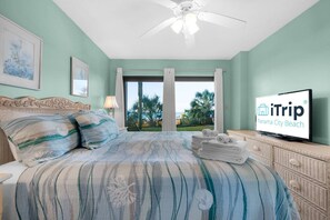 A bedroom with a bed, a television, and a view of palm trees.