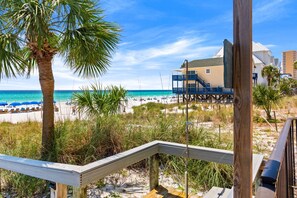 Blick auf einen Strand mit einer Holzterrasse, Palmen und einem Gebäude mit Balkon mit Meerblick.