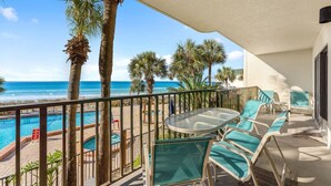 A balcony with a glass table and chairs, overlooking a pool and the ocean. - Family-friendly beachfront condo with private balcony, pool, and $300 of Free Activities Daily! (Panama City Beach)