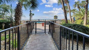 A pathway leading to a gated area with palm trees and a clear sky. - Family-friendly beachfront condo with private balcony, pool, and $300 of Free Activities Daily! (Panama City Beach)