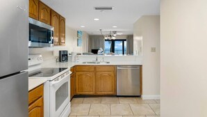 A modern kitchen with wooden cabinets, stainless steel appliances, and a view of the ocean. - Family-friendly beachfront condo with private balcony, pool, and $300 of Free Activities Daily! (Panama City Beach)