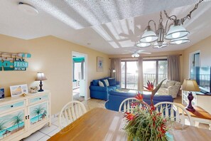 A living room with a dining table, blue sofa, and a ceiling fan.