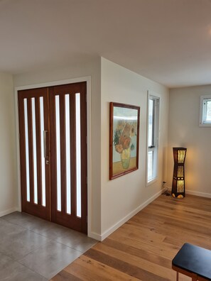 A room with a wooden floor, a large wooden door with vertical slats, a framed painting on the wall, and a floor lamp. - Pandora's Escape - Newly Built 7 Star Rated Home (Venus Bay)