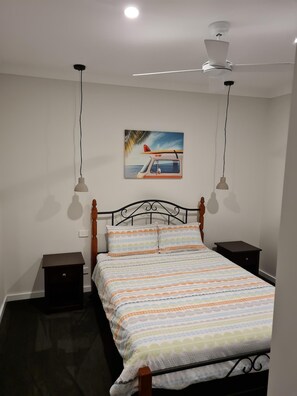A bedroom with a bed, a ceiling fan, two bedside tables, and a wall-mounted painting. - Pandora's Escape - Newly Built 7 Star Rated Home (Venus Bay)