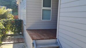 Ein Haus mit einer Holzdiele, einer Treppe zum Eingang und einem kleinen Garten mit Kies und Pflanzen.