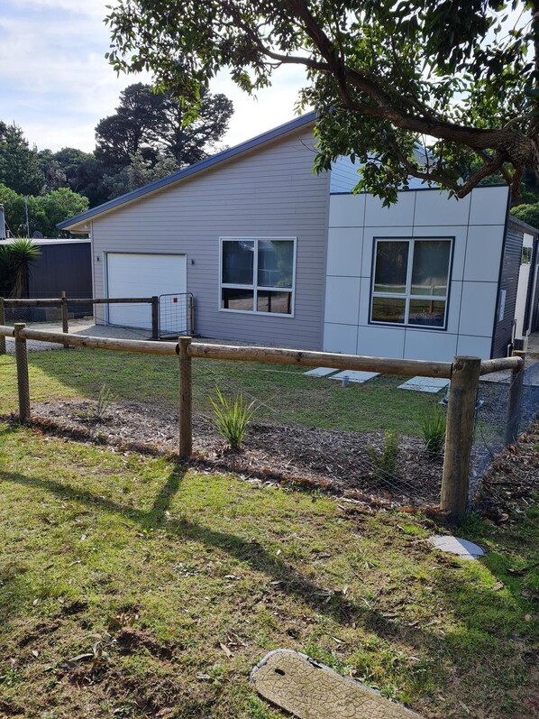 A modern two-story building with a garage, a fenced yard, and a tree in the foreground. - Pandora's Escape - Newly Built 7 Star Rated Home (Venus Bay)