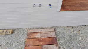 Eine weiße Außenwand mit drei Metallbeschlägen, einem Holzdeck und einem Kiesweg.