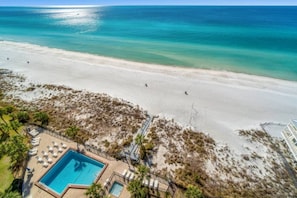 A beach resort with a swimming pool, lounge chairs, and a view of the ocean.