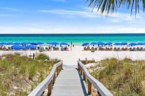 A wooden boardwalk leading to a beach with blue umbrellas and lounge chairs. - Beachfront 2BR | Free Beach Chairs, Hot Tub, Pool & $300 in Daily Activities! (Panama City Beach)