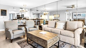 Un salon moderne avec un canapé, des fauteuils, une table basse et une cuisine en arrière-plan.
