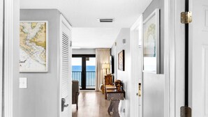 Un couloir avec une carte accrochée sur le mur de gauche, une vue sur la mer par une porte vitrée et un banc en bois.