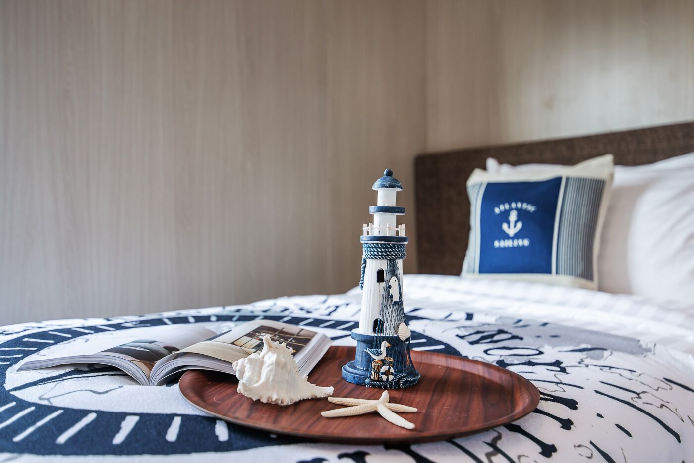 Un lit avec une couvre-lit aux motifs marins, une petite maquette de phare, un coquillage et une étoile de mer, le tout disposé sur un plateau en bois.