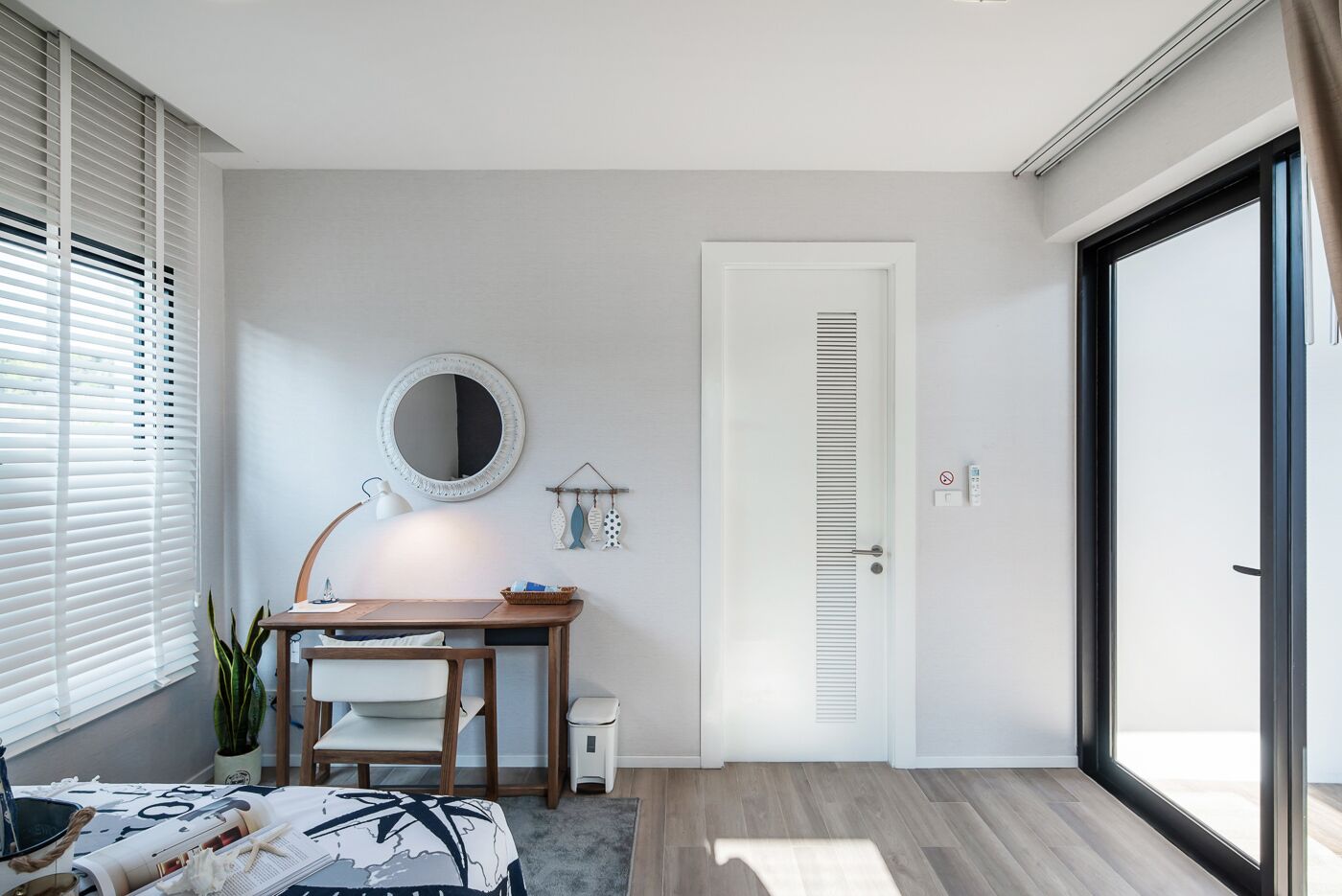 A modern bedroom with a wooden desk, a round mirror, and a sliding glass door.