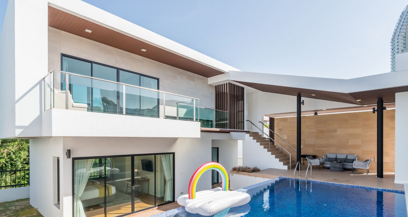 Ein modernes, zweistöckiges Haus mit Pool, Glastüren und einer überdachten Sitzgelegenheit im Freien.