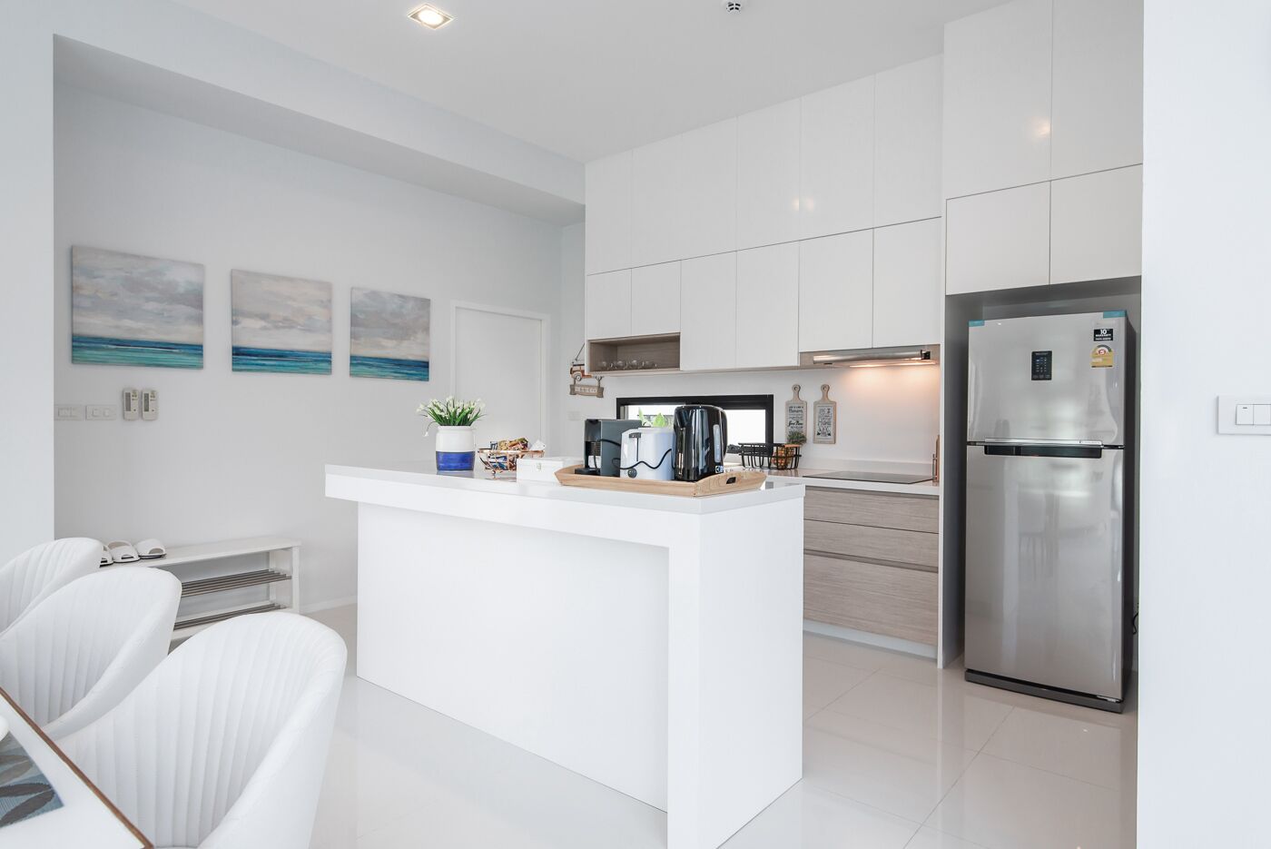 A modern kitchen with white cabinetry, a stainless steel refrigerator, and a central island with a coffee maker and decorative items.