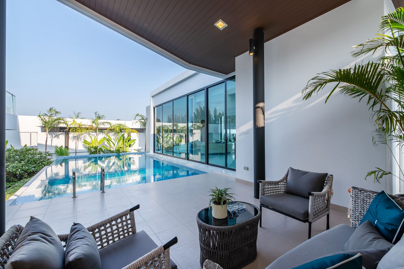 A modern outdoor pool area with wicker furniture and a glass wall overlooking a residential neighborhood.