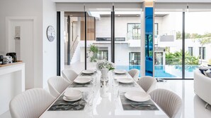 Uma zona de refeições moderna com uma mesa comprida posta para seis pessoas, janelas amplas e vista para uma piscina e área externa.